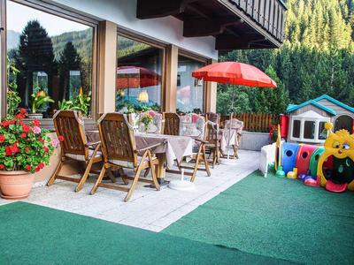 Terrasse mit Gartentisch und Stühlen, bunte Spielsachen und grüne Hecke im Hintergrund.