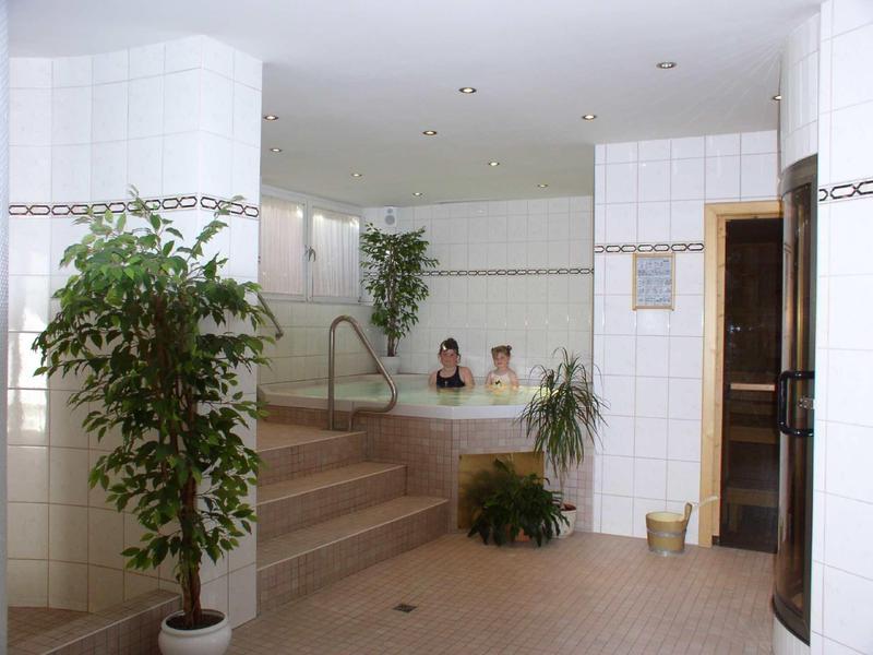 Helles Badezimmer mit weißen Fliesen, Pflanzen und zwei Personen im Whirlpool.