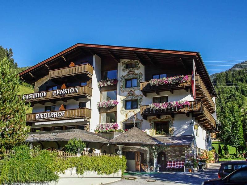 Traditionelles Alpenhaus mit Holzbalkonen und bunten Blumen unter klarem blauem Himmel.