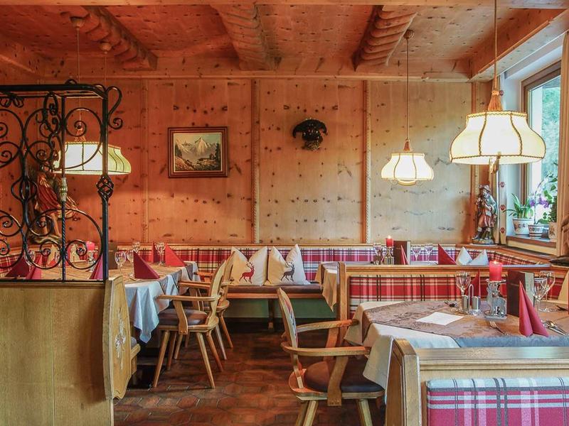 Gemütlicher Gastraum mit Holzwänden, karierten Sitzpolstern und gedeckten Tischen in warmem Licht.