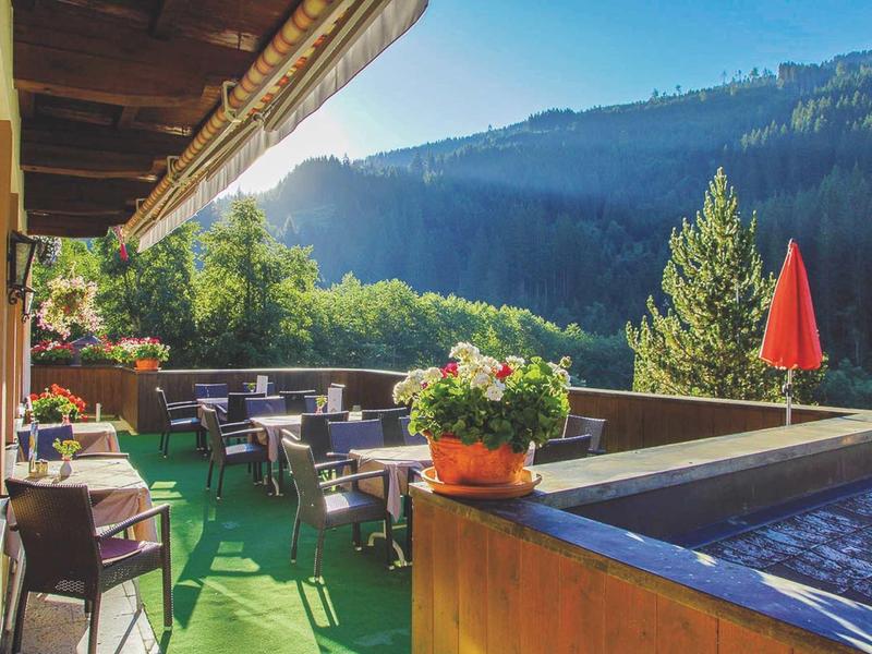 Balkon mit Tischen, Stühlen, Blumen und Berglandschaft im Hintergrund bei Sonnenschein.