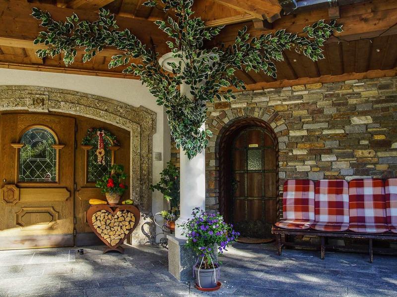 Rustikaler Hauseingang mit Holzbank, steinverkleideter Wand und Säule mit Kletterpflanze.