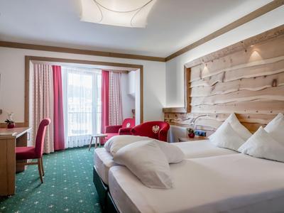 Habitación de hotel luminosa con cama doble, zona de estar y ventana grande con vistas a un balcón.