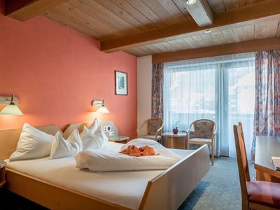 Gemütliches Schlafzimmer mit Doppelbett, Holzmöbeln, oranger Wand und Balkon mit Tageslicht.