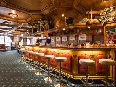 Interior de un bar de hotel acogedor con mostrador de madera, taburetes rojos y luz cálida.