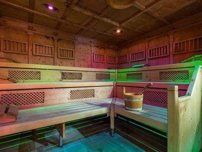 Saunaraum mit hölzernen Sitzbänken, Eimer und warmen, bunten Beleuchtungseffekten.
