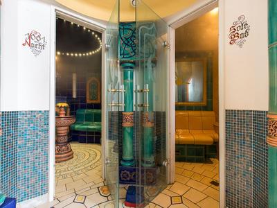 Eingangsbereich mit Glasdrehtür, türkisen Kacheln, gelben Bänken und warmem Licht.