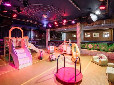 Bunt beleuchteter Indoor-Spielplatz mit Rutsche, Karussell und weichem Mattenboden.