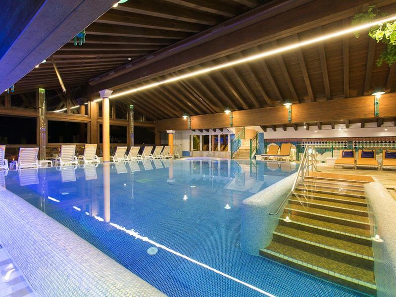 Innenpool mit Holzdecke, Treppe ins Wasser, Liegestühlen und entspannter Beleuchtung.