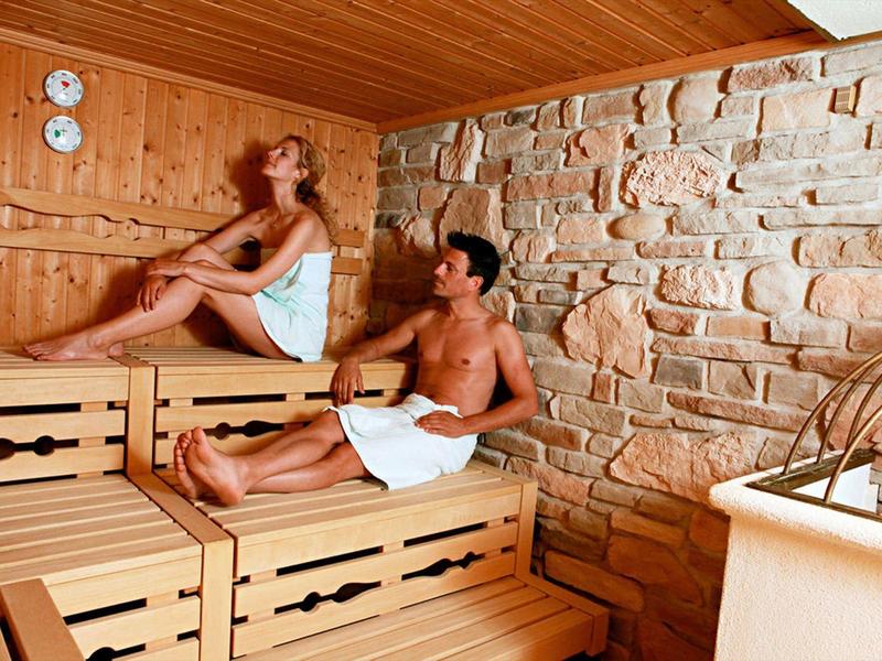 Zwei Personen entspannen in einer Sauna mit Holz- und Steinwänden.