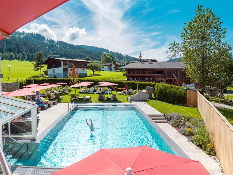 Pool mit Sonnenschirmen neben einem Hotel mit Bergblick unter blauem Himmel