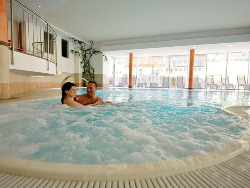 Zwei Personen entspannen in einem runden, sprudelnden Whirlpool in einem hellen Wellnessbereich.