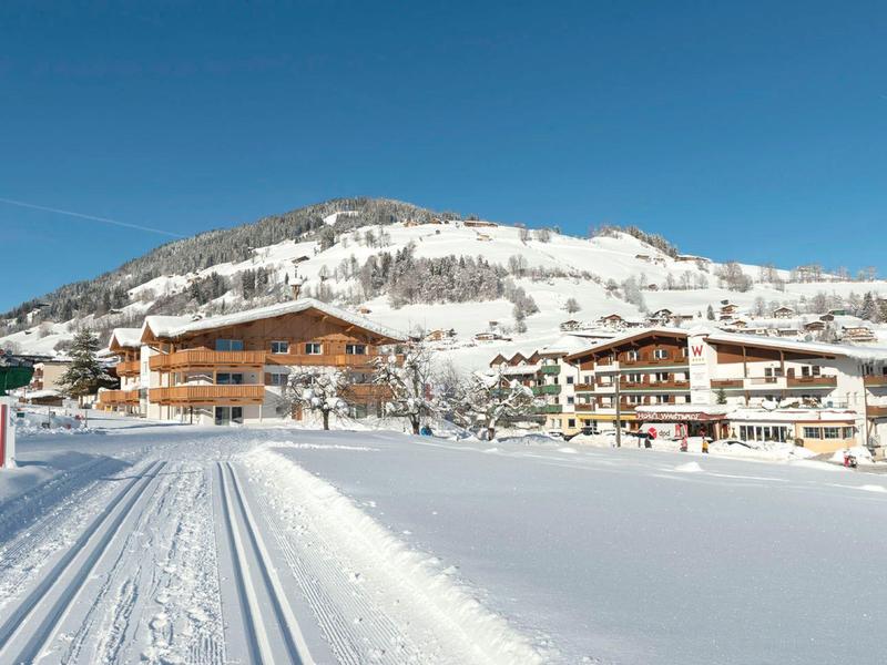Verschneite Winterlandschaft mit Hotels vor einem schneebedeckten Berg unter klarem blauem Himmel.