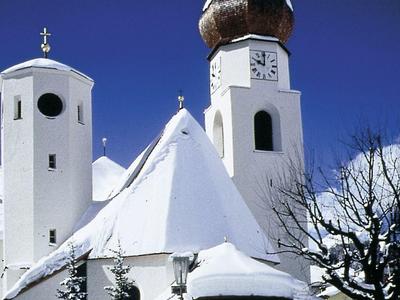 Weiße Kirche mit Zwiebelturm, verschneiten Dächern und klarem blauem Himmel im Winter.