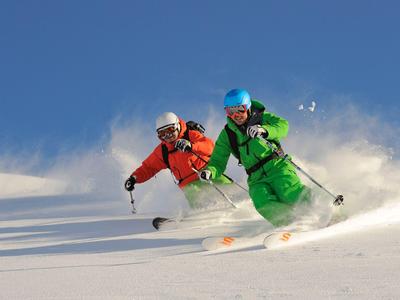 Deux skieurs en tenues colorées descendent une neige fraîche sous un ciel clair.