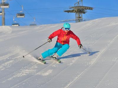 Skieur en veste rouge et pantalon bleu descendant une piste fraîchement damée.
