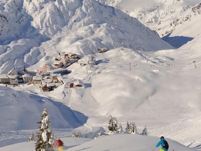 Schneebedeckte Berge mit Skifahrern und kleinen Nadelbäumen bei klarem Himmel.