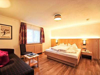 Gemütliches Schlafzimmer mit Doppelbett, Sofa, Holzboden und warmem Licht.