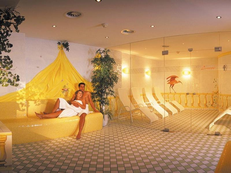 Großer Wellnessraum mit warmem Licht, Pflanzen, Liegen und Gelbtönen für entspannte Atmosphäre.