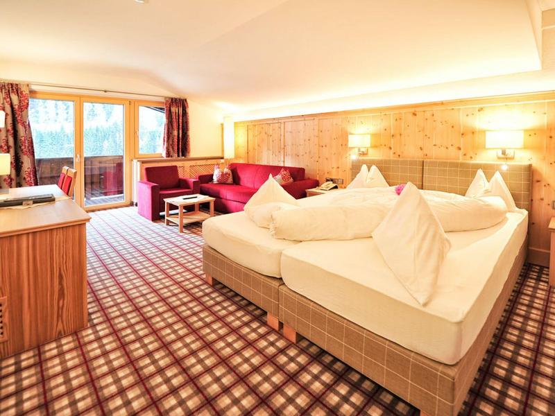 Helles Hotelzimmer mit Holzmöbeln, großem Bett, Sofa, Teppichboden und Balkon mit Aussicht.