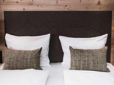 Zwei weiße Betten mit braunen Kissen und dunklem Kopfteil vor hellbrauner Holzverkleidung.