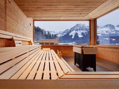 Moderne Sauna mit Holzinterieur und großer Panoramafensteransicht auf verschneite Berge.