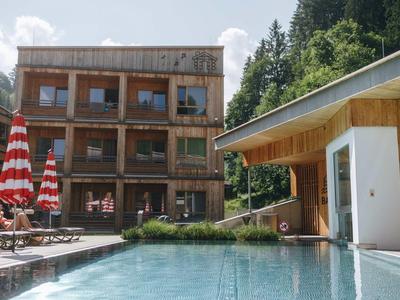 Modern chalet with terrace and pool in a mountainous area with green trees.