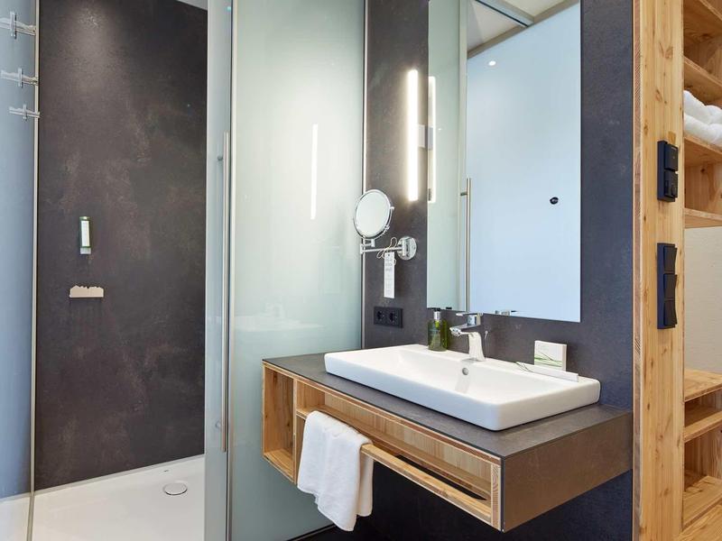 Modernes Badezimmer mit eckiger Waschschüssel, Glasdusche, Holzregal und dunklen Wandfliesen.