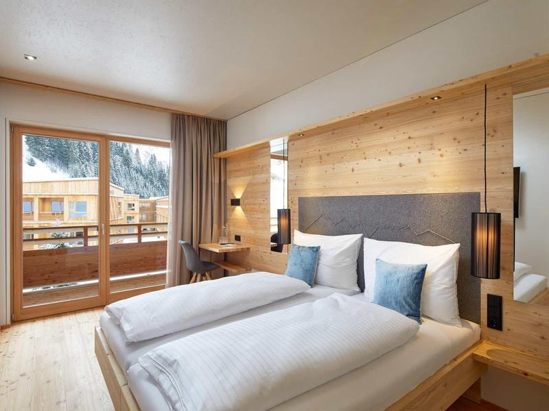 Modernes Schlafzimmer mit großem Fenster, Holzwänden und gemütlichem Doppelbett mit weißen Kissen.