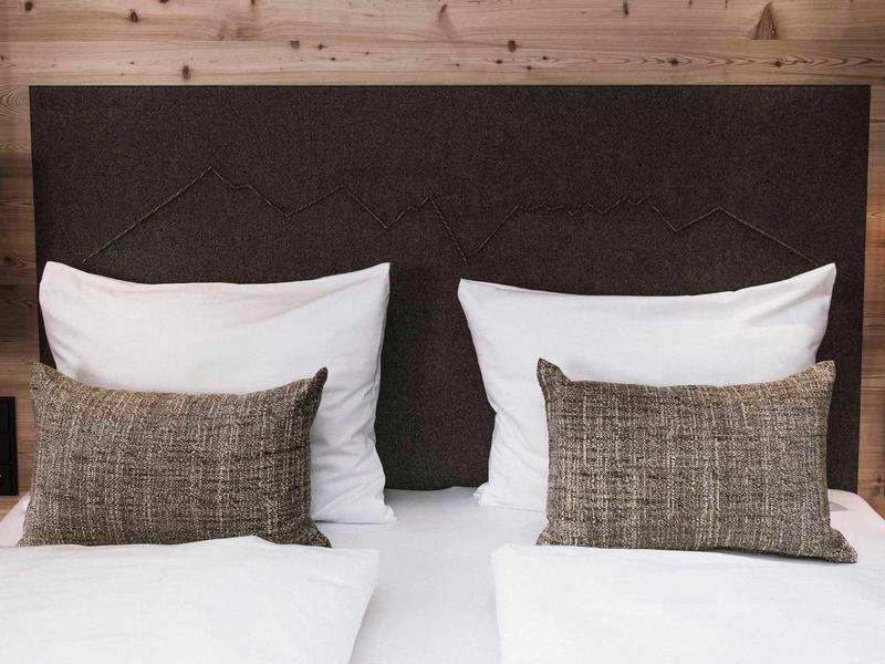 Zwei weiße Betten mit braunen Kissen und dunklem Kopfteil vor hellbrauner Holzverkleidung.