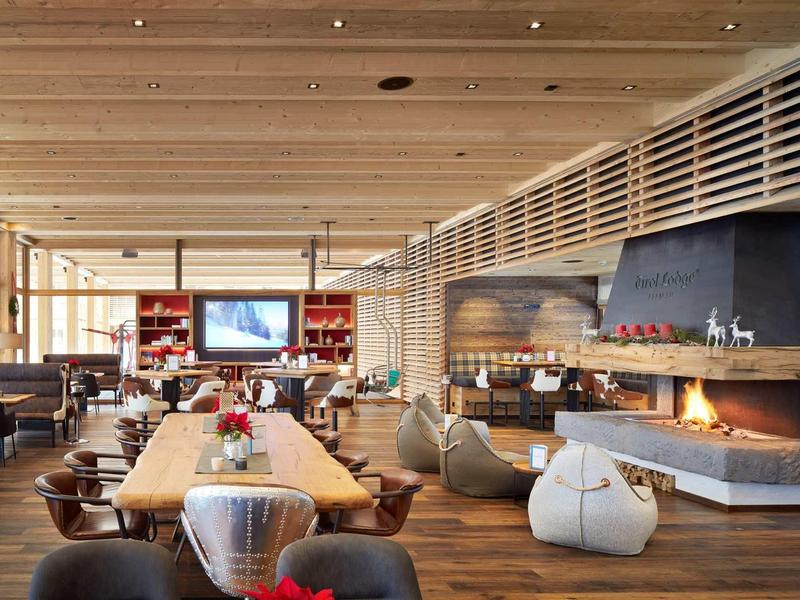 Modernes Restaurant mit Holzdecke, Kamin, langen Holztischen und Sitzsäcken in warmem Licht.