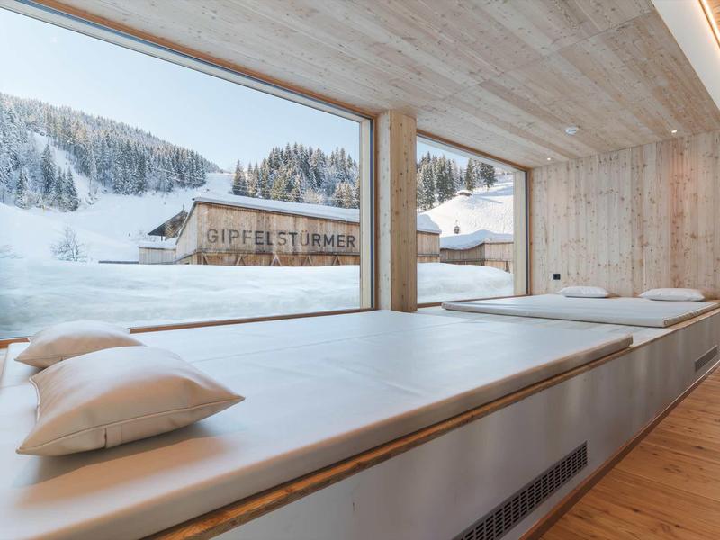 Helles, modernes Zimmer mit großen Fenstern, Holzwänden und einer langen Sitzbank mit Kissen.