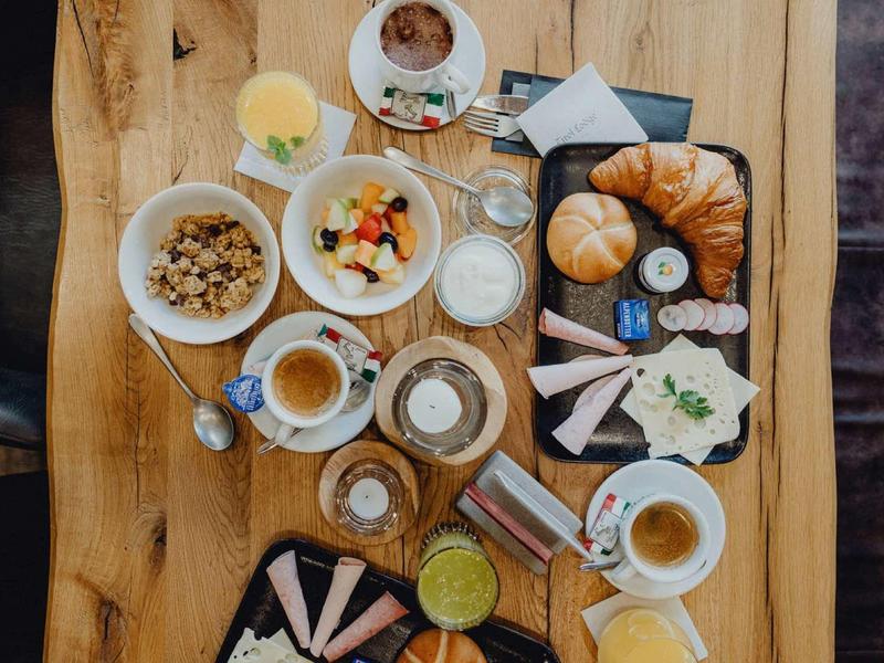 Frühstück mit Müsli, Obst, Croissants, Kaffee und Aufschnitt auf rustikalem Holztisch.