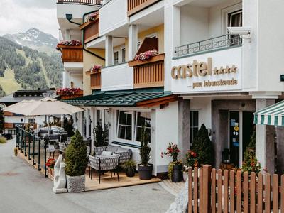 Vnější pohled na hotel s balkony, posezením a horskou krajinou v pozadí.