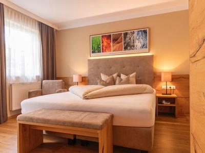 Gemütliches Schlafzimmer mit großem Bett, Holzmöbeln, warmem Licht und Fenstervorhängen.