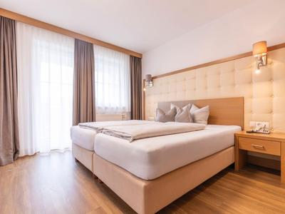 Moderní hotelový pokoj se dvěma oddělenými postelemi, dřevěnou podlahou a teplými béžovými tóny.