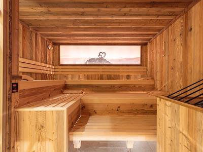 Sauna aus hellem Holz mit mehrstufigen Sitzbänken und Fenster für Tageslicht.