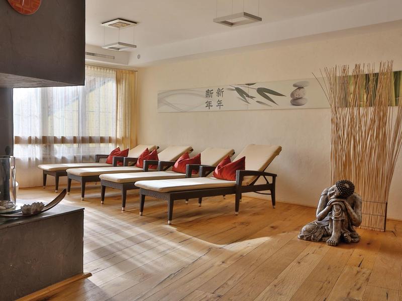 Helles, modernes Wohnzimmer mit Holzboden, drei Liegestühlen, roten Kissen und Deko-Elementen.