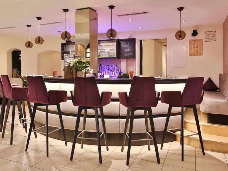 Moderner Innenraum mit Bartresen und lila Stühlen, heller Raum mit Pendelleuchten und alter Fernseher.