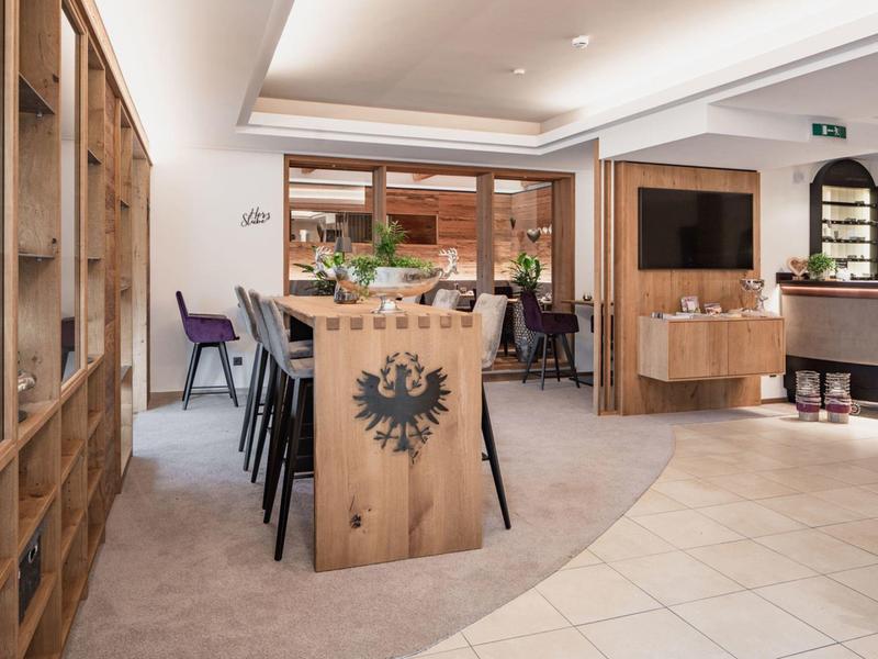 Moderner Raum mit Holzmöbeln, hohen Stühlen und hellen Fliesenboden, helle Beleuchtung.