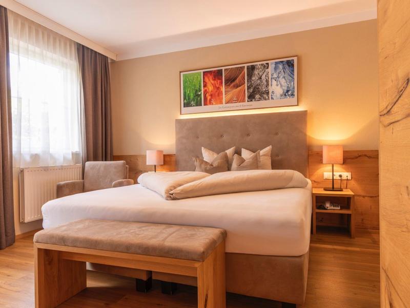 Gemütliches Schlafzimmer mit großem Bett, Holzmöbeln, warmem Licht und Fenstervorhängen.