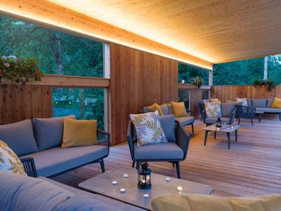 Cozy lounge area with armchairs and sofas on a wooden terrace under a lit roof.