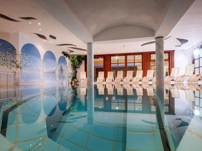 Innenbereich eines Schwimmbads mit klarem Wasser, Säulen und weißen Liegestühlen an der Seite.