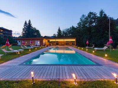 Illuminated outdoor pool with sun loungers and trees in a hotel garden at dusk.