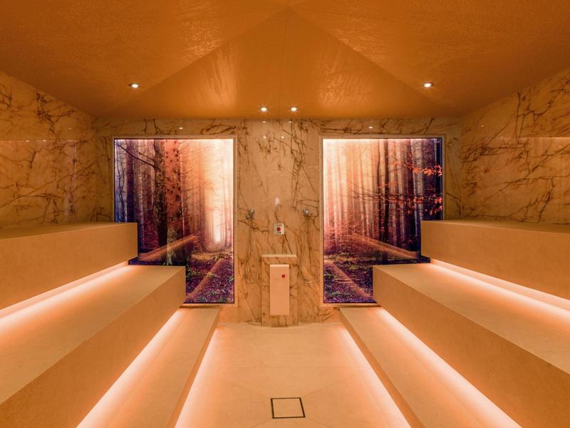 Moderne Sauna mit Sitzbänken und beleuchteten Stufen, dekoriert mit Waldmotiven an der Wand