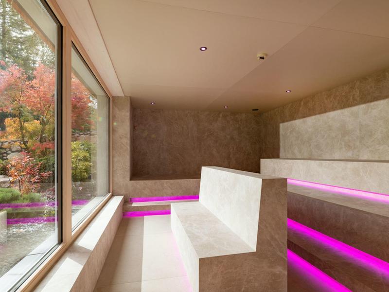 Moderner Wellnessbereich mit Sitzstufen und lila LED-Beleuchtung neben großem Fenster mit Blick ins Grüne