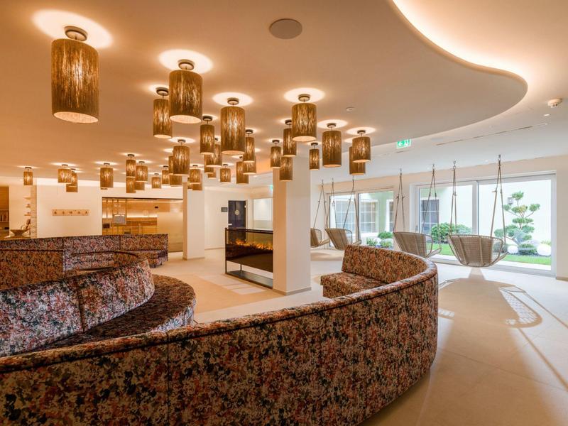 Moderne Hotellobby mit geschwungenen Sofa, eleganten Leuchten und großen Fenstern mit Blick ins Grüne
