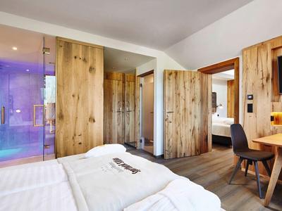 Moderner Hotelzimmer mit Holzmöbeln, Doppelbett, türkis beleuchtetem Bad und Arbeitsplatz mit Stuhl.