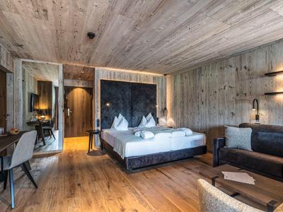 Modernes Schlafzimmer mit Holzwänden, Doppelbett, dunklem Sofa, Schreibtisch und warmem Licht.