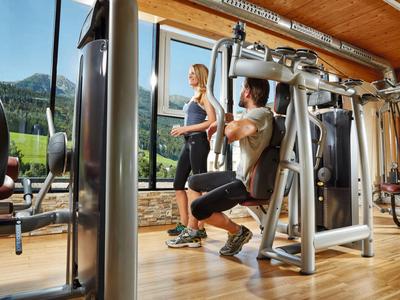 Personen trainieren Beine an einer Fitnessmaschinen im sonnigen Fitnessstudio mit Bergblick.